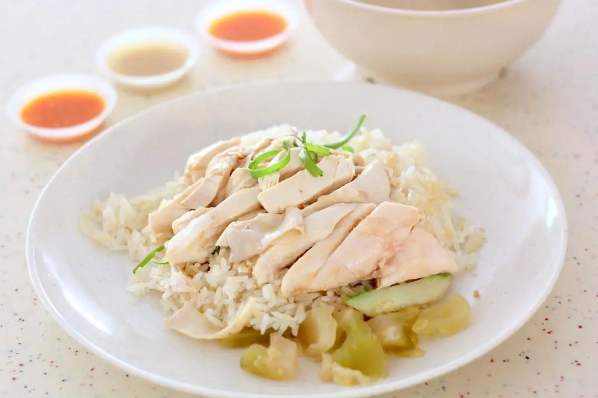 Singapore Chicken Rice: Steamed chicken with fragrant rice cooked with chicken stock mixed with shallots, ginger, and garlic, served with pickles, sliced cucumber, garlic chili sauce, ginger sauce, and black soy sauce