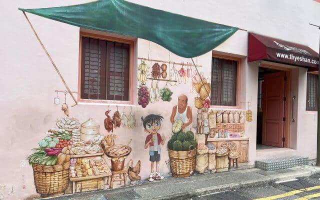 Charming street mural in Singapore's Chinatown featuring a young detective reminiscent of 'Detective Conan' beside a traditional vendor, with baskets of durians and fresh produce, and a canopy overhead.