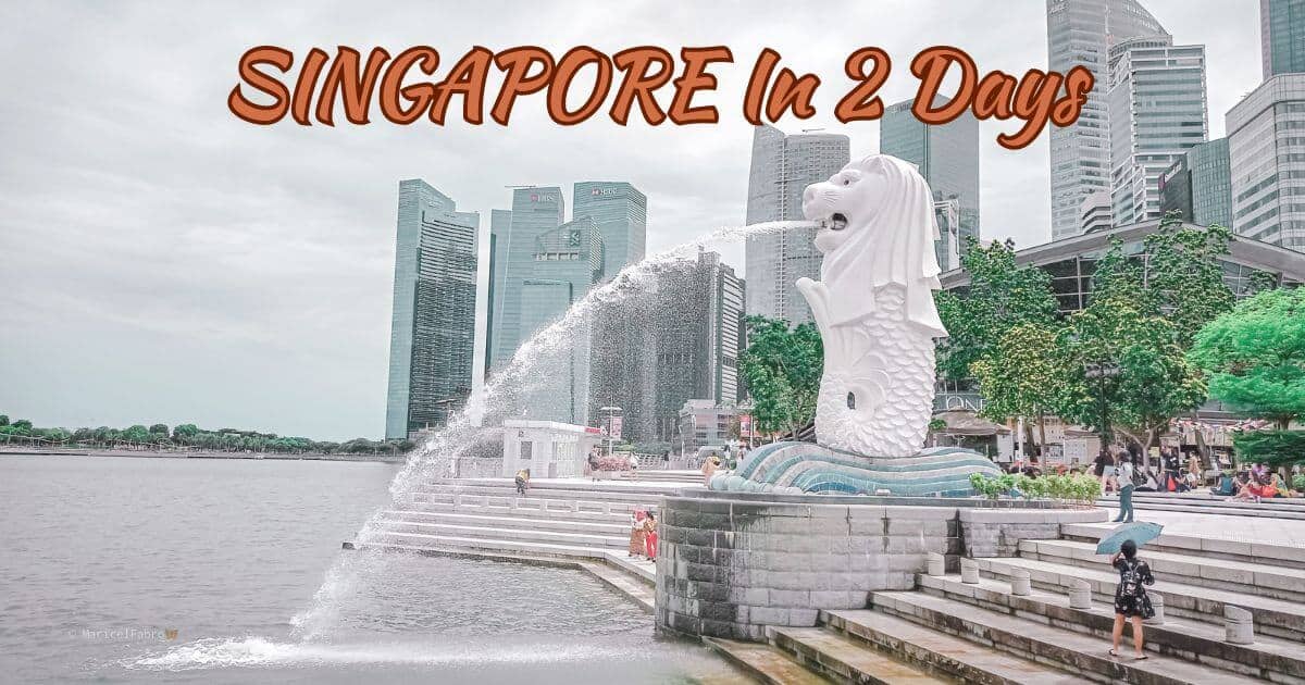 A bustling scene at the Merlion Park in Singapore with the iconic Merlion statue spouting water into the Marina Bay. Skyscrapers rise in the background while visitors wander the promenade. One of the must visit place for a Singapore in 2 days visit.