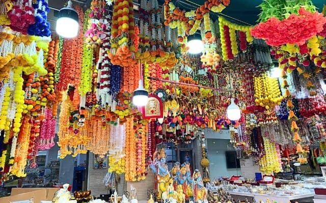 A store in Singapore's Little India teems with a vibrant array of hanging floral garlands and religious artifacts. The festive decorations and lit lanterns create a lively and colorful atmosphere, inviting shoppers to explore the cultural merchandise.