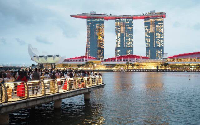 Dusk view of the iconic Marina Bay Sands hotel and the ArtScience Museum in Singapore, with visitors on the boardwalk enjoying the skyline and reflections on the water.