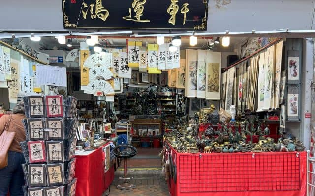 A traditional souvenir shop in Singapore's Chinatown, displaying an array of Chinese calligraphy, paintings, and cultural figurines under a signboard with Chinese characters.