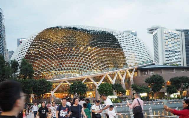 Evening at the waterfront with the distinctive durian-shaped Esplanade Theatres on the Bay, Singapore, bustling with people in the foreground enjoying the city's cultural scene.