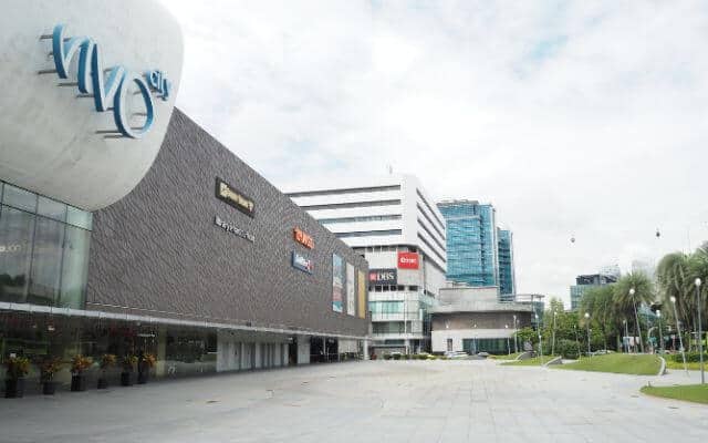 Exterior view of Vivo City Mall, Singapore's largest shopping mall, featuring a distinctive modern façade with the mall's logo prominently displayed, and a spacious, empty plaza leading up to the entrance.