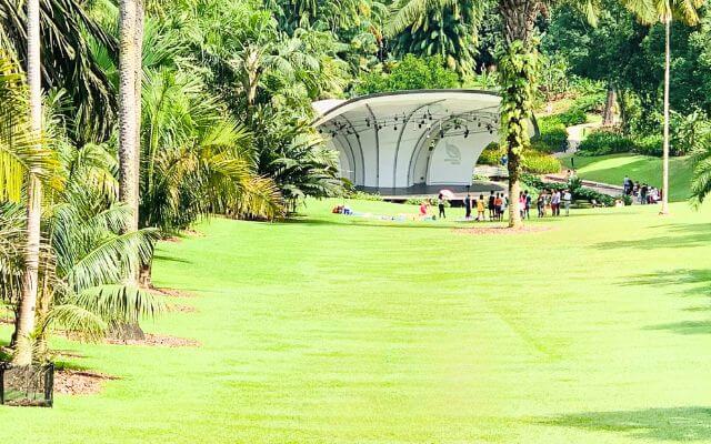 The Shaw Foundation Symphony Stage at the Singapore Botanic Gardens, nestled amid lush palm trees and a sprawling green lawn, setting the scene for a serene concert in the park.