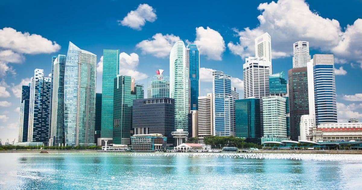A stunning view of Singapore's Marina Bay skyline, featuring modern skyscrapers with glass facades reflecting in the water under a bright blue sky with scattered clouds - Best Time To Visit Singapore