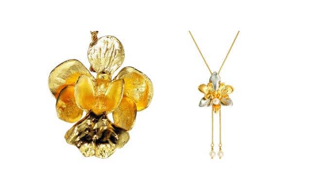 Two pieces of gold-plated orchid jewelry. On the left, a detailed gold-plated orchid pendant showcases realistic petals with a shiny, textured finish. On the right, a more delicate orchid-inspired necklace features a smaller orchid pendant with gold and silver tones, accented by two dangling pearls on thin chains.
