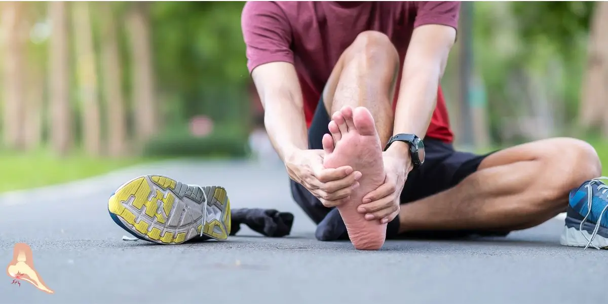 A person sitting on a path, visibly in extreme pain as they hold the bottom of their bare foot, suffering from plantar fasciitis after walking. This highlights the severe discomfort that can occur while traveling, emphasizing the importance of proper footwears such as wide toe box shoes in preventing plantar fasciitis.