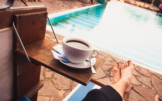 A person relaxing by a poolside, with their bare feet propped up on a lounge chair, soothing tired feet.