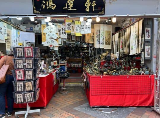 A vibrant souvenir shop in Singapore's Chinatown, featuring tables covered with red cloths displaying various items like figurines, calligraphy sets, and traditional Chinese art.