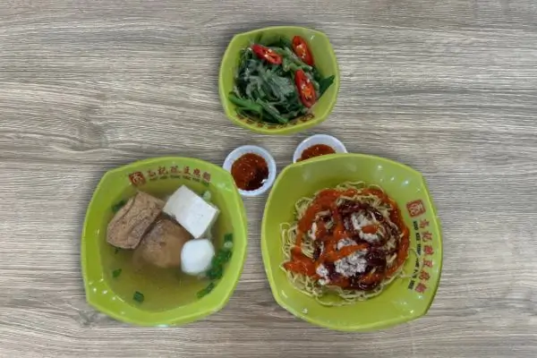 Yong Tau Foo meal. One bowl has soup with tofu, fish balls, and vegetables in clear broth. Another features dry noodles with minced meats and savory sauce, while the third holds fresh boiled kang kong, and side condiments like chili and sweet sauce.