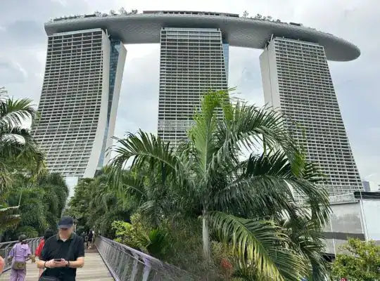Marina Bay Sands hotel in Singapore viewed from a garden walkway, with tropical greenery and the iconic three-tower structure above.